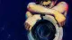 A cropped figure locks both arms around a washing machine door, symbolizing the strain of carrying a